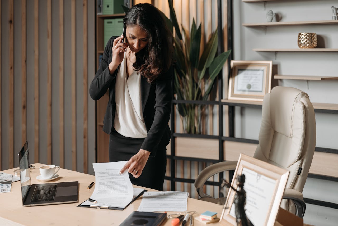 brand-01 A female lawyer talking on phone while reviewing legal documents in a modern office setting.