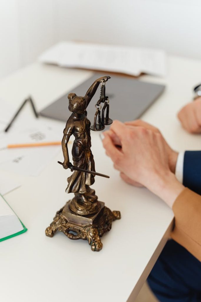close-up-shot-of-a-lady-justice-figurine-on-a-white-table-7876148 Bronze Lady Justice statue on a white office desk with hands in the background. Symbol of law and fairness.