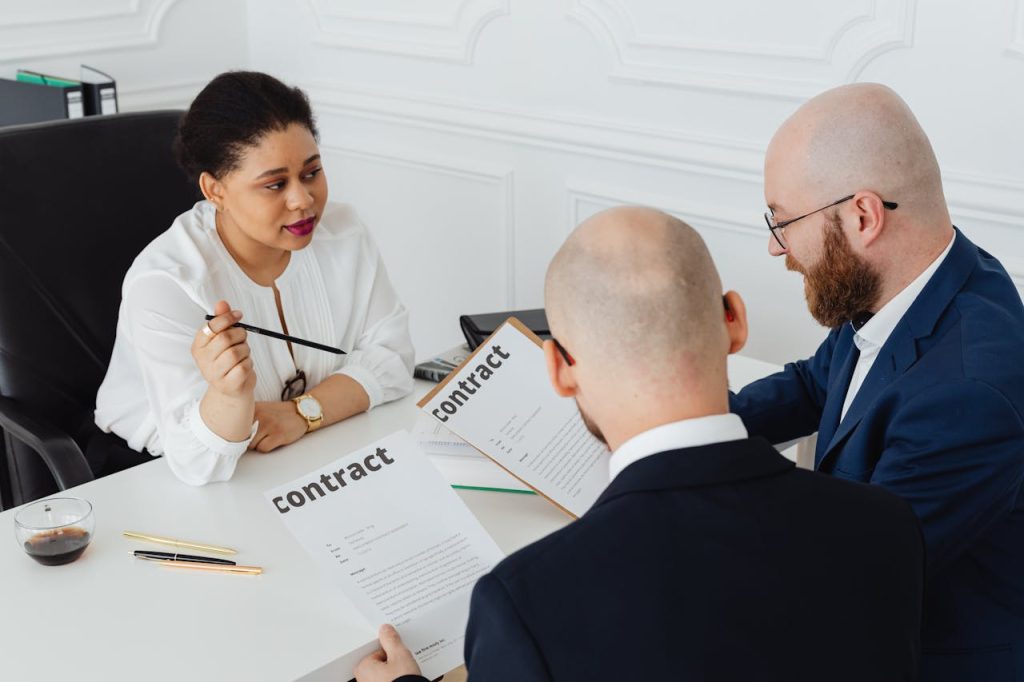 woman-sitting-while-explaining-the-contracts-7876001 Three business professionals in discussion over a contract in a modern office setting.